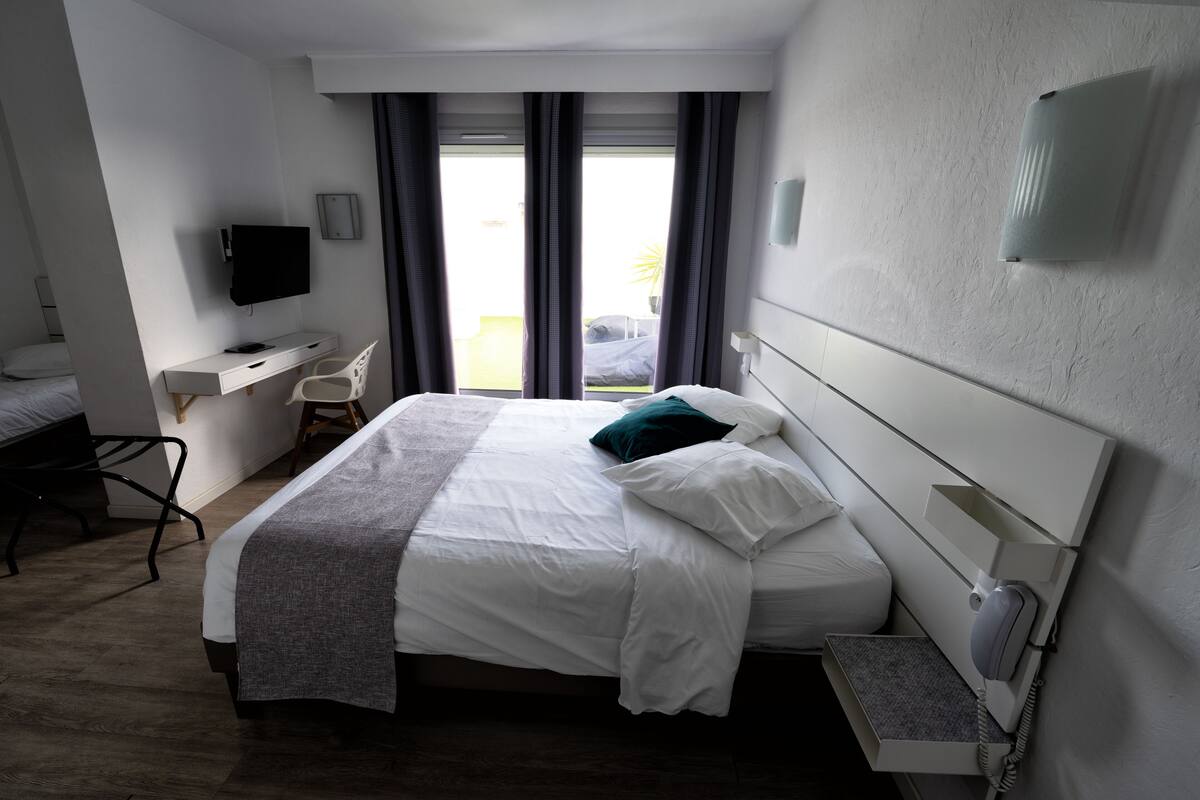 Une chambre d’hôtel équipée d’un lit, d’un bureau, d’une chaise, d’une télévision et d’une fenêtre avec des rideaux.