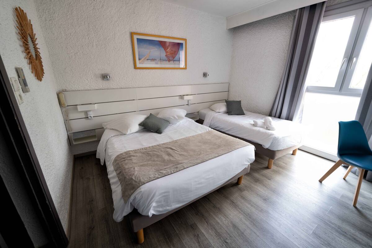 Une chambre d’hôtel avec deux lits, une grande fenêtre et un tableau au mur.