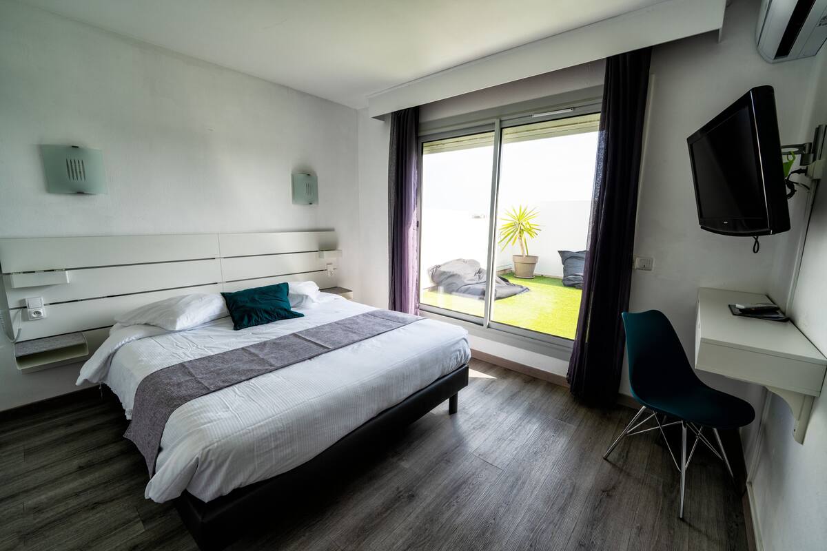 Une chambre d’hôtel moderne dotée d’un grand lit, d’un bureau, d’une chaise, d’une télévision et d’un balcon avec vue.