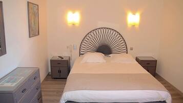 Una cama bien hecha con un cabecero original, dos mesitas de noche con lámparas, un aparador y un cuadro enmarcado en la pared.