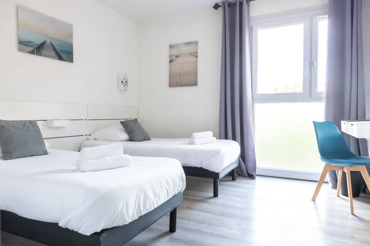 Une chambre d’hôtel avec deux lits, un bureau et une chaise.