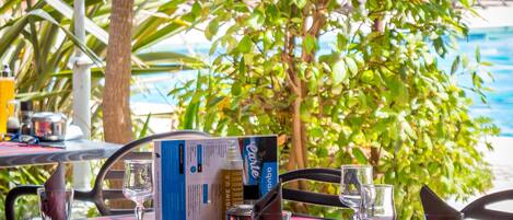 A table set with a menu, glasses, and a bottle, near a poolside with lush greenery.