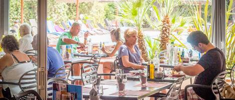 An outdoor restaurant with tables and chairs, palm trees, and a view of the outdoors.