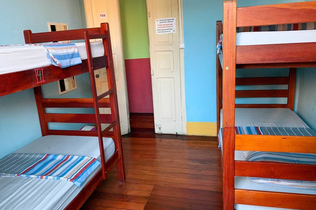 Une chambre de dortoir avec des lits superposés, des meubles en bois et une porte sur laquelle est apposée une pancarte.