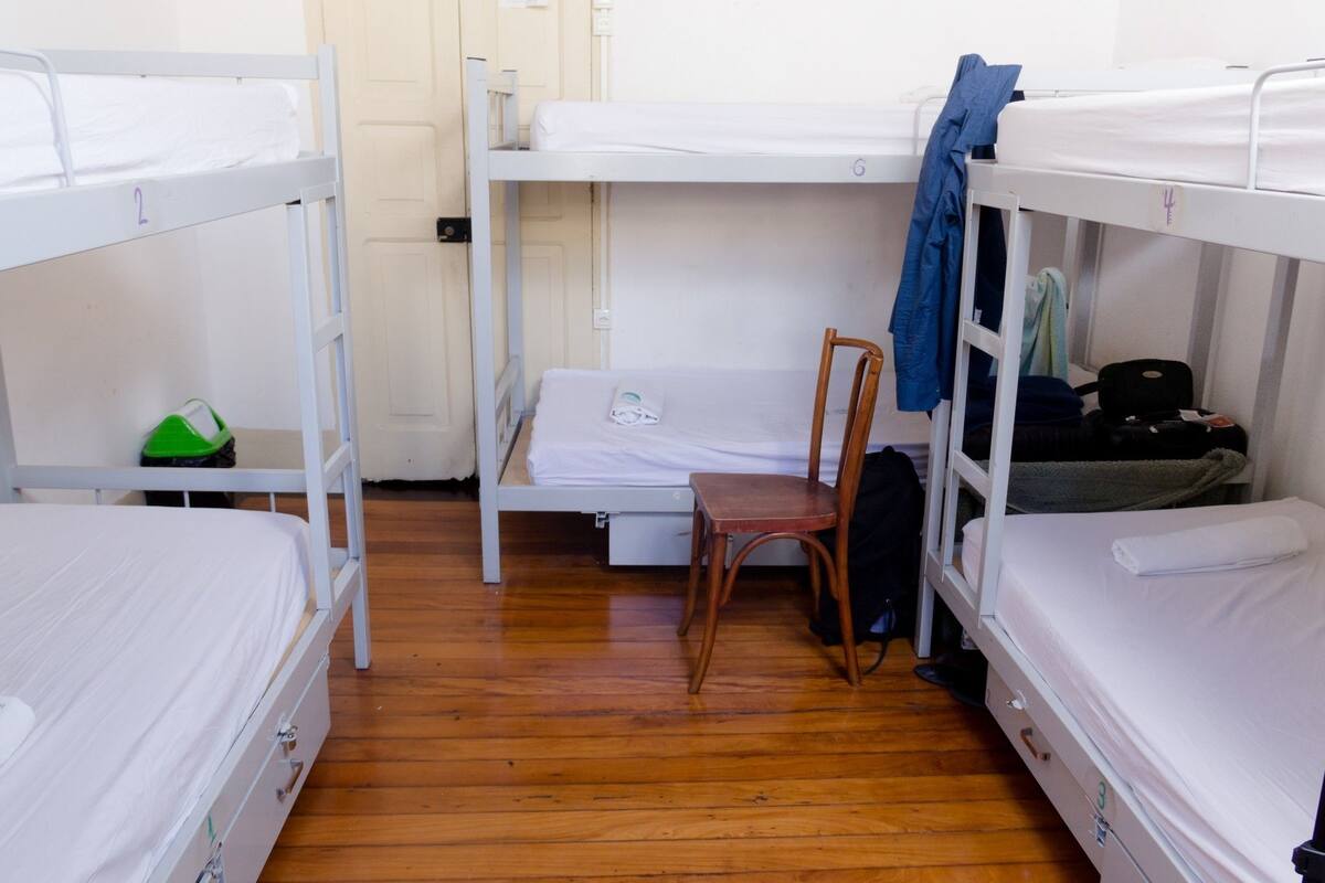 Une chambre de dortoir avec des lits superposés, une chaise en bois, une valise verte et une valise noire.