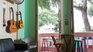 A room with a green wall, a black leather couch, two guitars, a wooden chair, and a balcony with red stools. - Massape Rio Hostel (Rio de Janeiro)