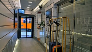 Un vestíbulo de hotel con una pared de vidrio, un carrito de equipaje y una pantalla digital mostrando una vista de habitación.