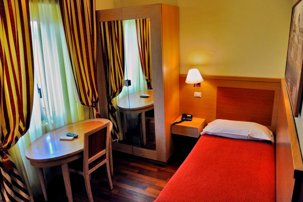 Ein Hotelzimmer mit Bett, Schreibtisch mit Stuhl, Spiegel, Lampe und Telefon.