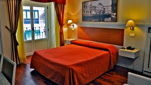 Una habitación de hotel con cama, mesita de noche, lámpara, teléfono y ventana con cortinas.