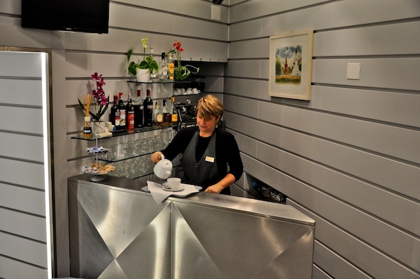 A modern bar area with a stainless steel counter, shelves with bottles and flowers, and a painting on the wall. - Hotel Rio (Milan)