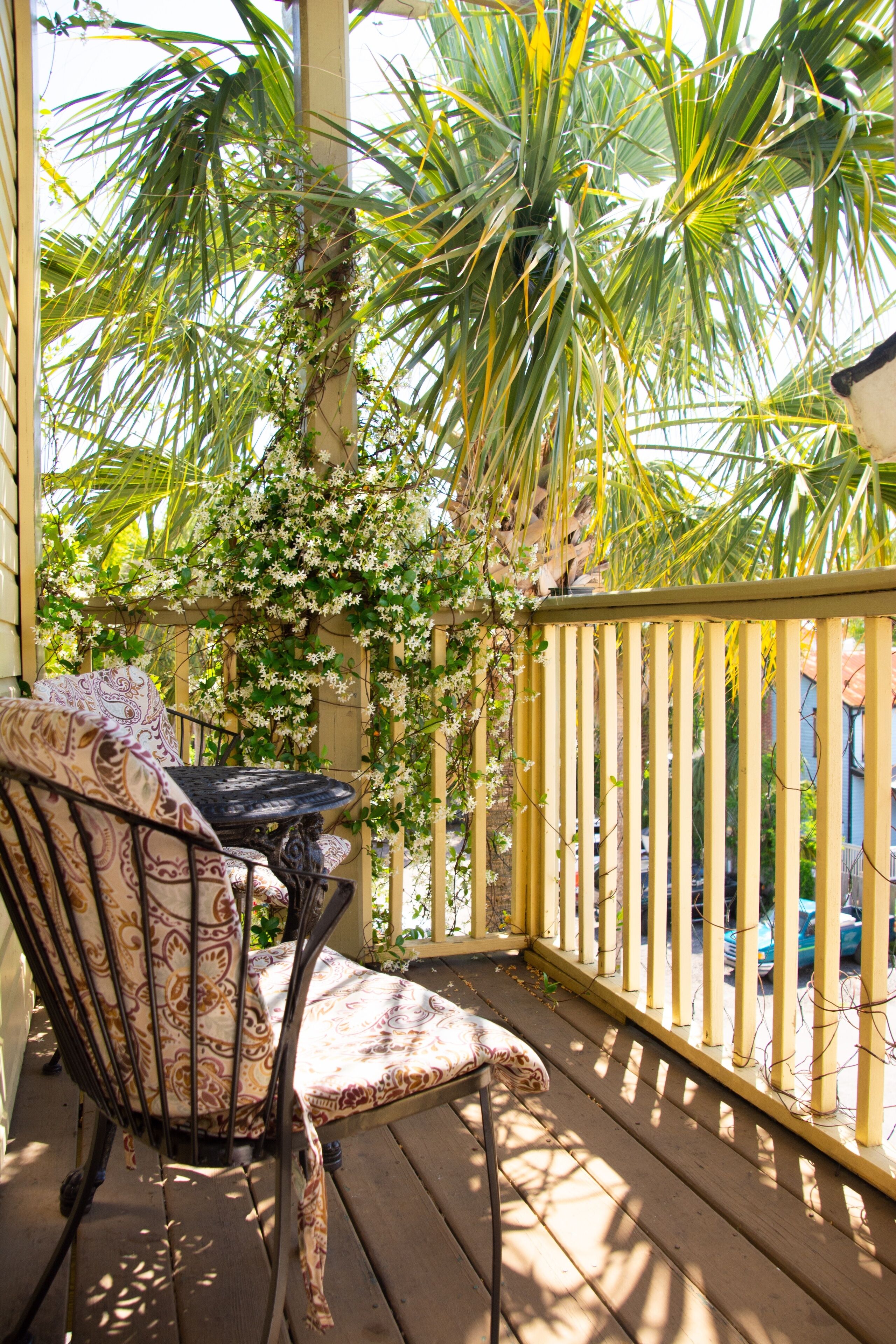 A wooden deck with a chair and a table, surrounded by a yellow railing and lush greenery.
