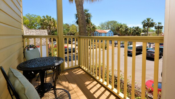 A wooden deck with a metal table and chairs, a yellow railing, and a view of parked cars and palm trees. - Agustin Inn (St. Augustine)
