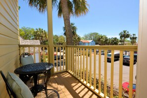 A wooden deck with a metal table and chairs, a yellow railing, and a view of parked cars and palm trees. - Agustin Inn (St. Augustine)