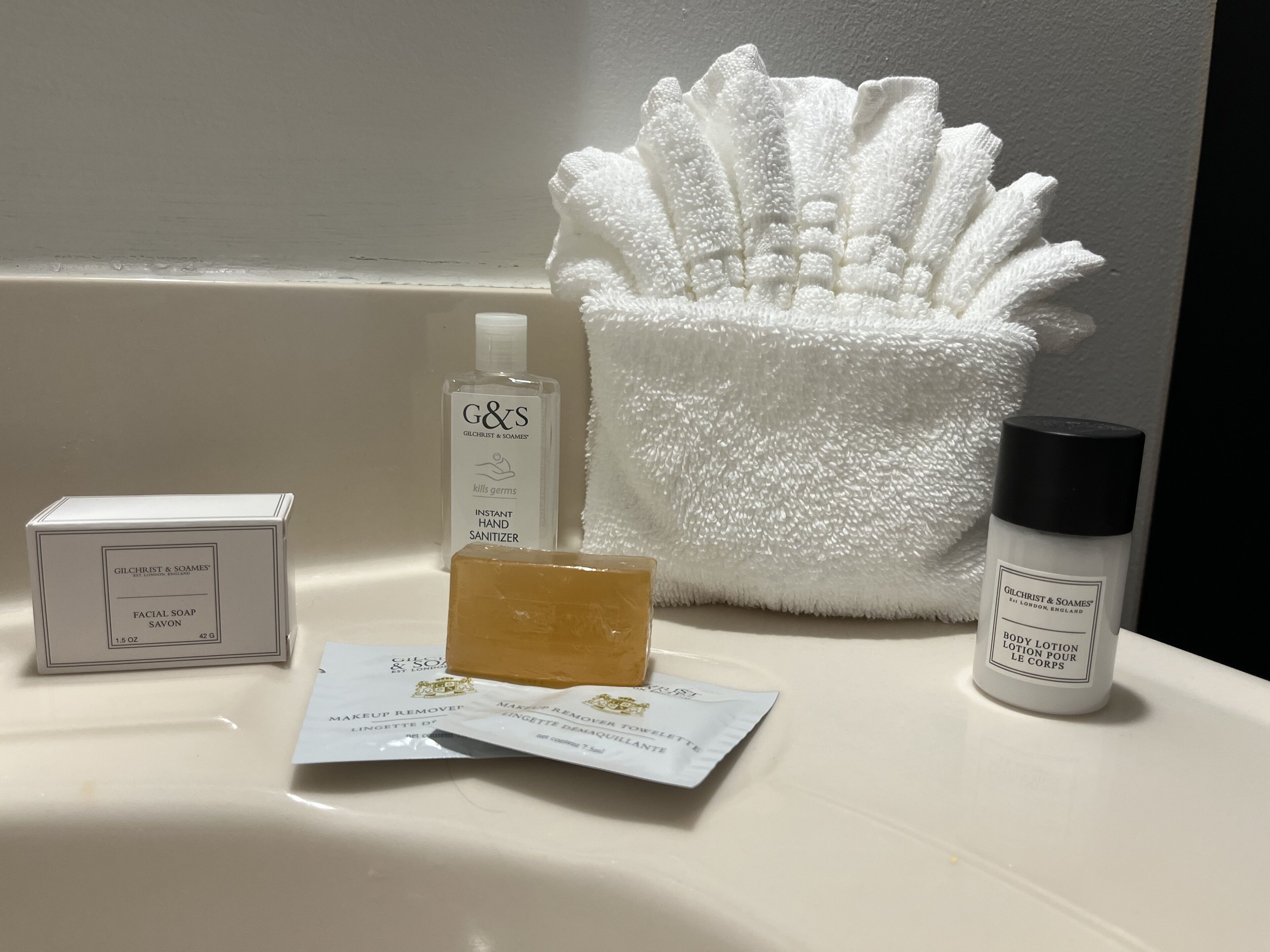 Ein Waschbecken mit Seife, Handdesinfektionsmittel, einer Make-up-Entfernungs-Packung und einer Bodylotion-Flasche.