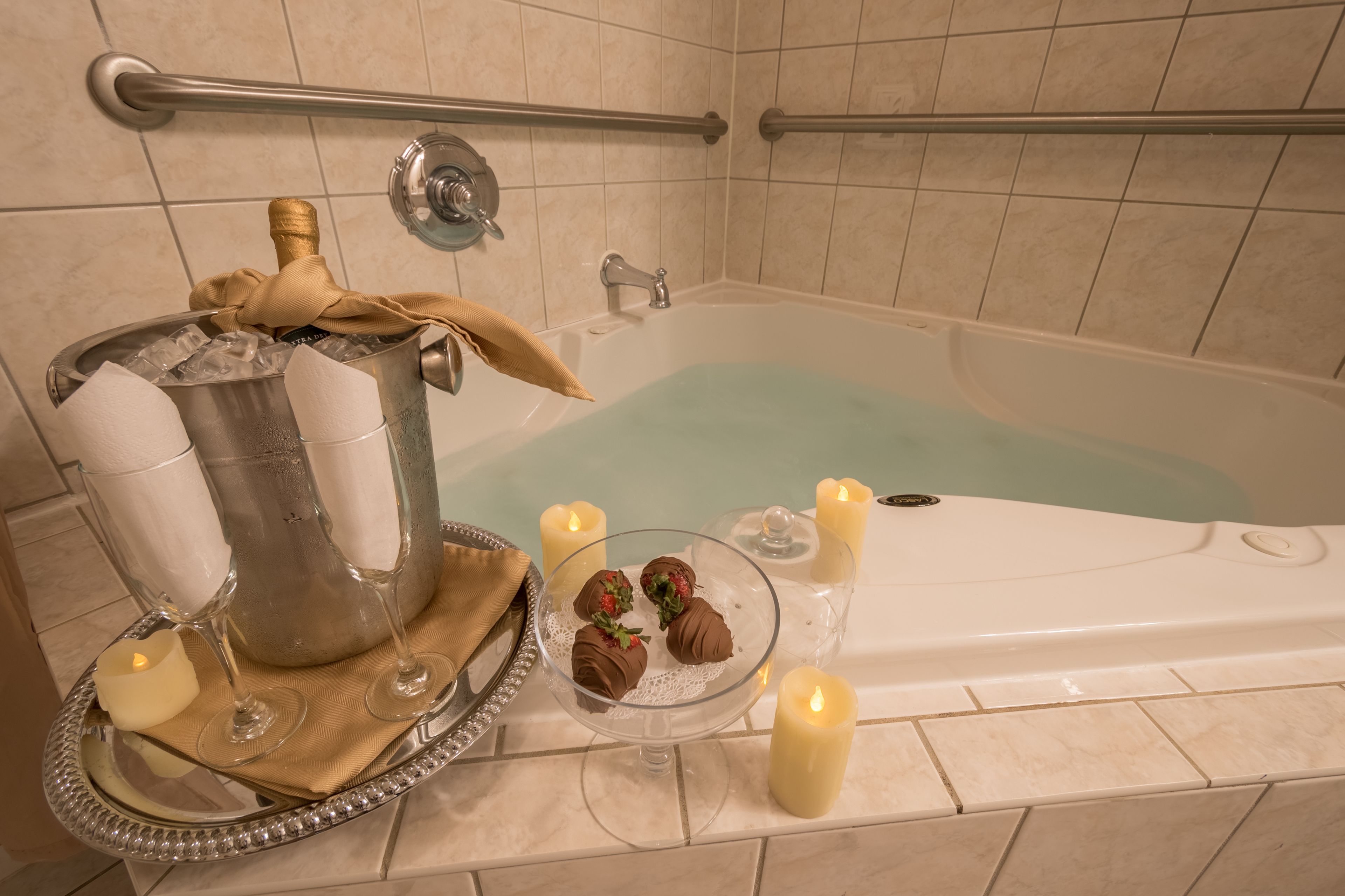 A bathroom with a bathtub, a metal bucket, candles, and chocolate-covered strawberries on a glass plate.