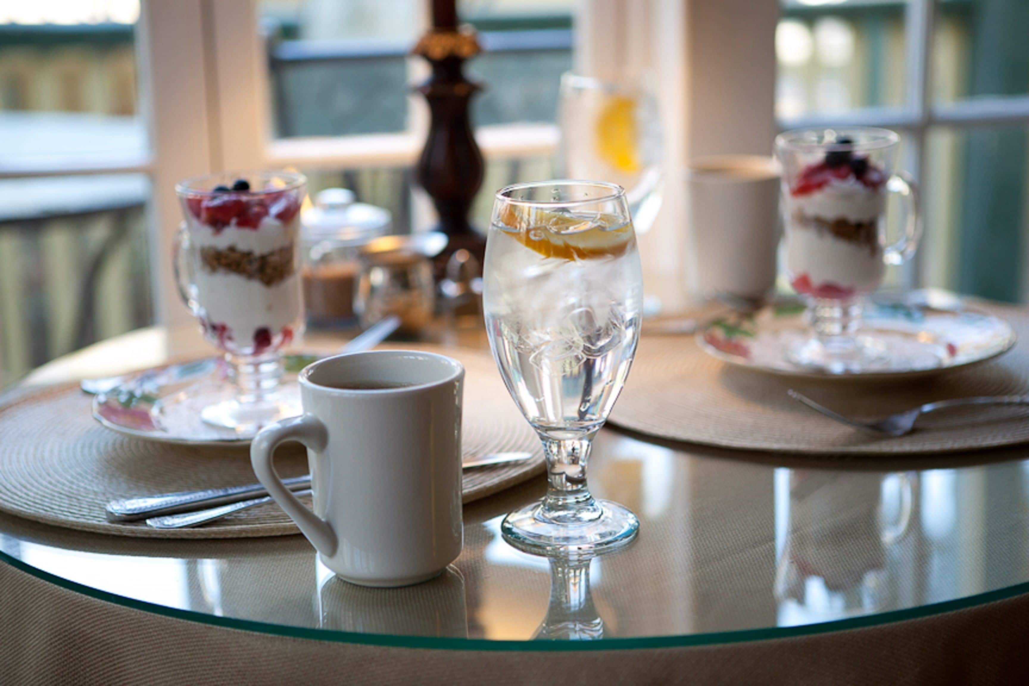 A table with a glass dessert dish, a white mug, and a glass of iced tea.