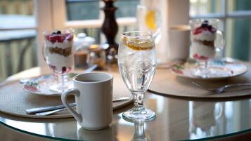 Una mesa con un postre en un recipiente de vidrio, una taza blanca y un vaso de té helado.