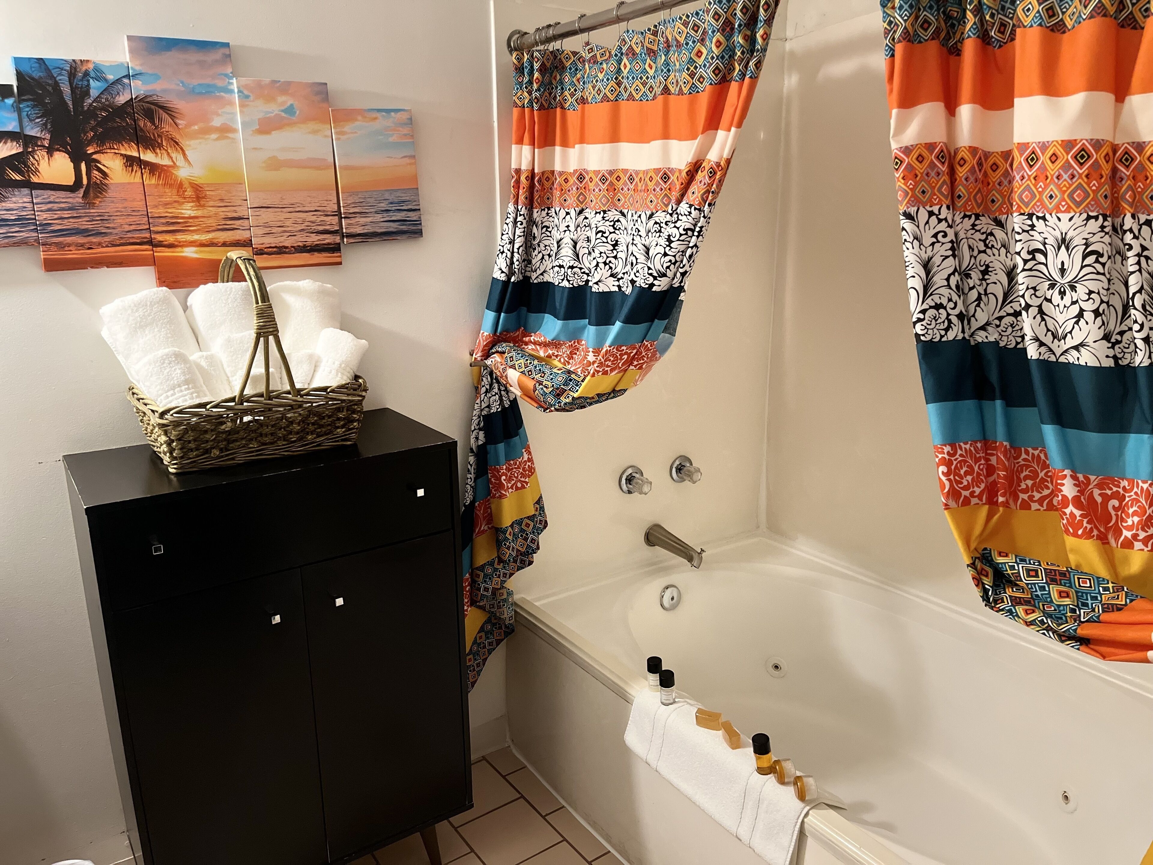 Un baño con una bañera, un mueble negro con toallas y una cortina de ducha decorativa.