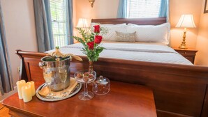 A neatly made bed with white linens, a vase with red roses, a champagne bucket, and a tray with glasses and a cake on a wooden table. - Agustin Inn (St. Augustine)