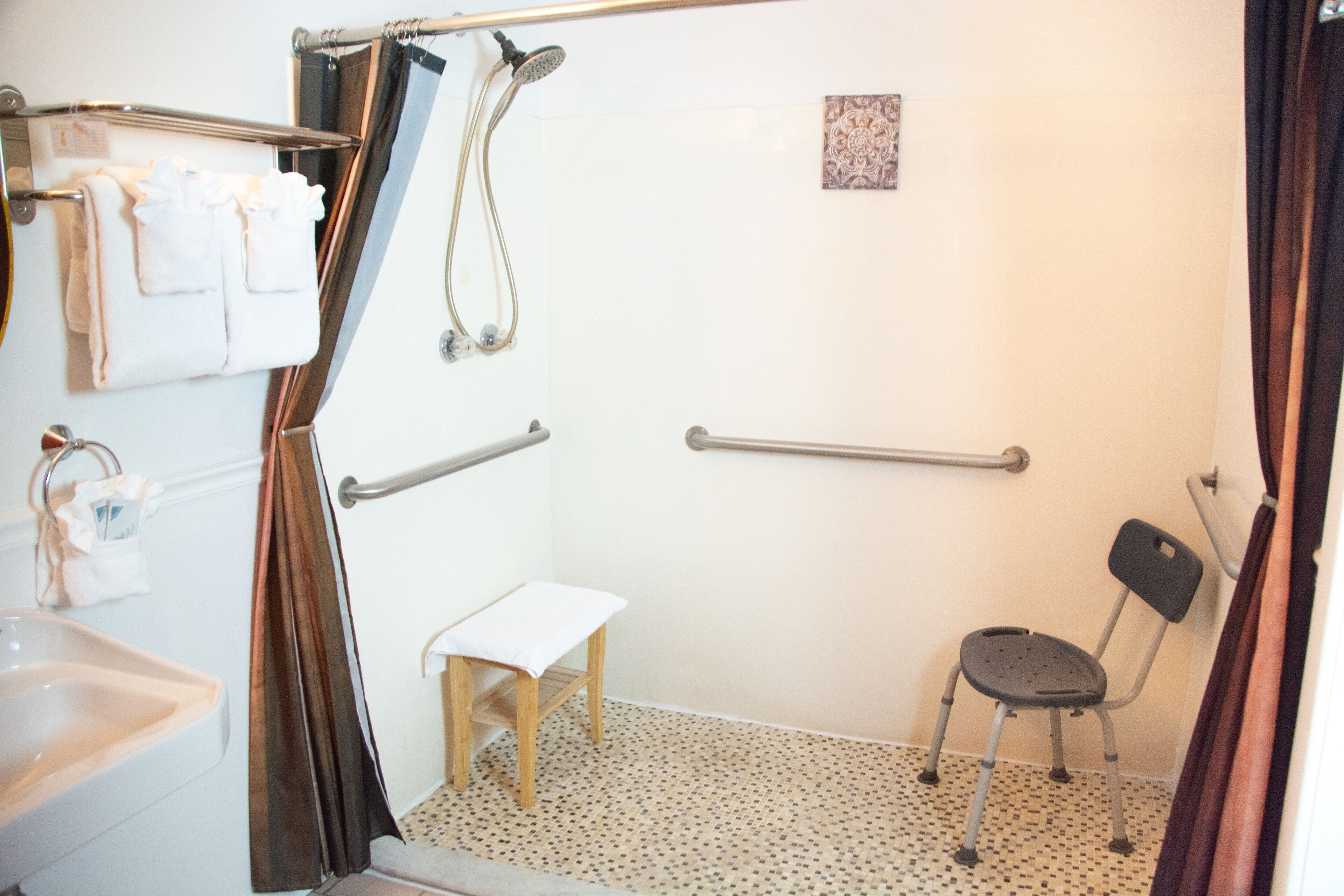 A bathroom with a shower, a sink, a small stool, and a chair.