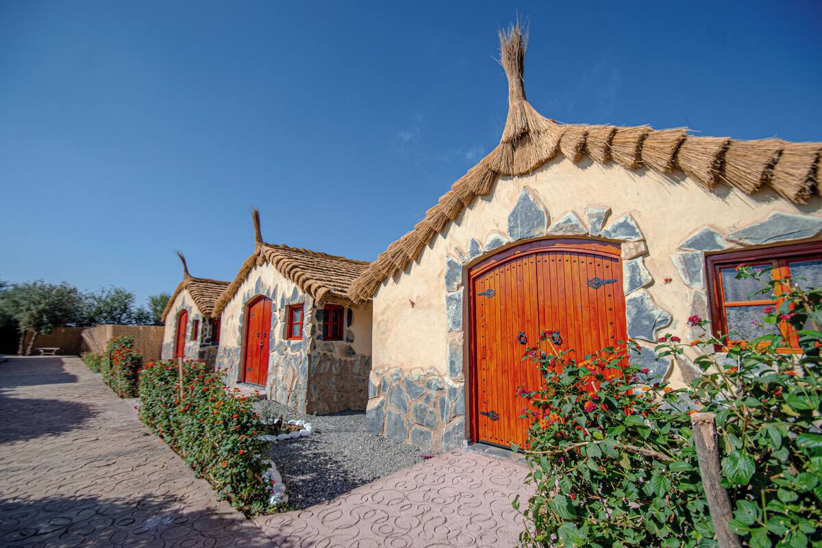 A row of traditional buildings with thatched roofs and stone walls, featuring large wooden doors and a paved pathway.