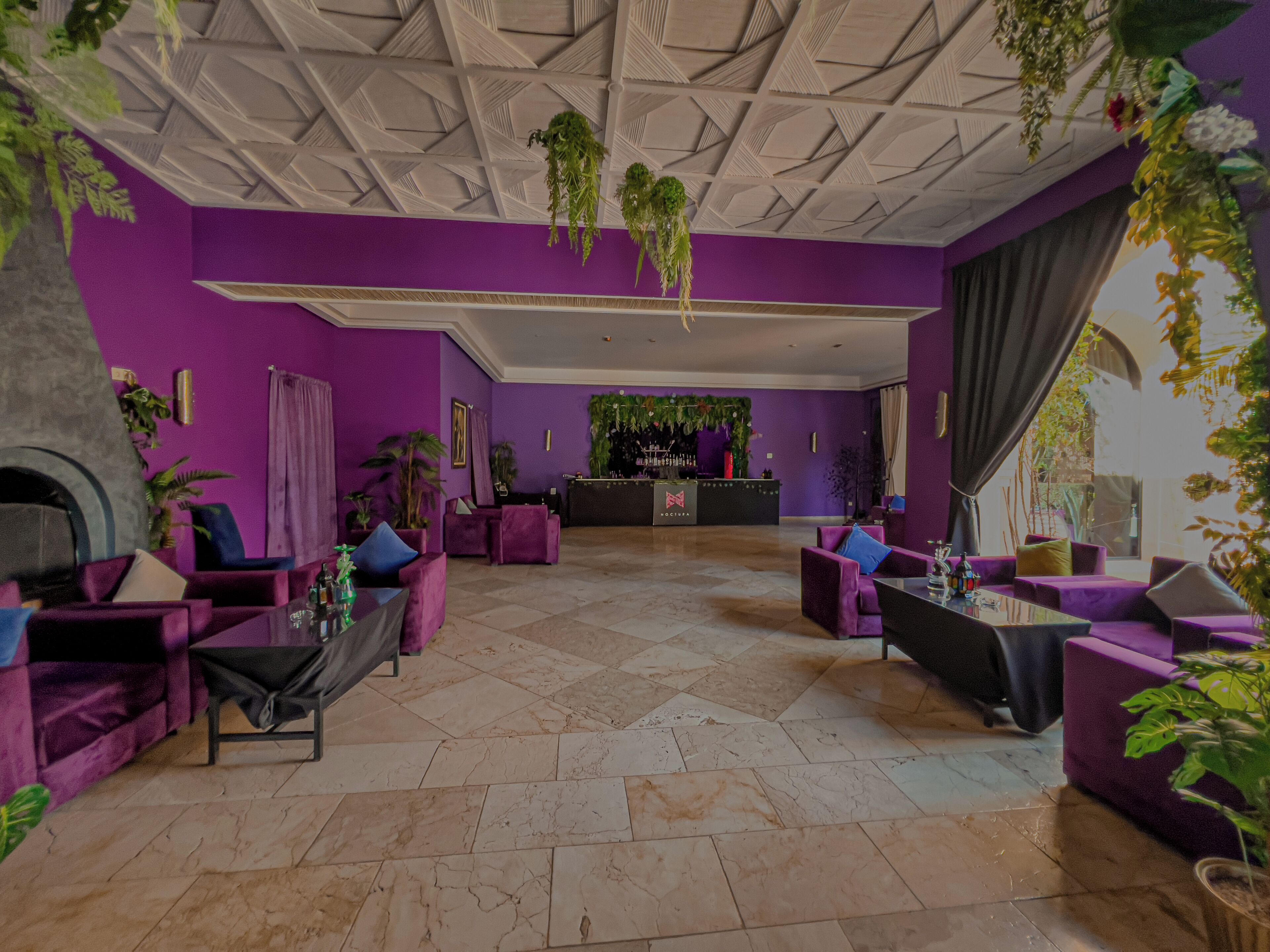 Een moderne lobby met paarse muren, een open haard en een bar.