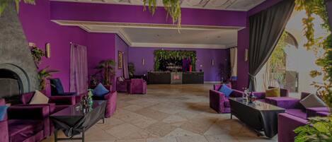 Een moderne lobby met paarse muren, een open haard en een bar.