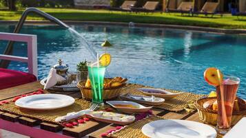 A poolside dining setup with a table, plates, glasses, and a water fountain.