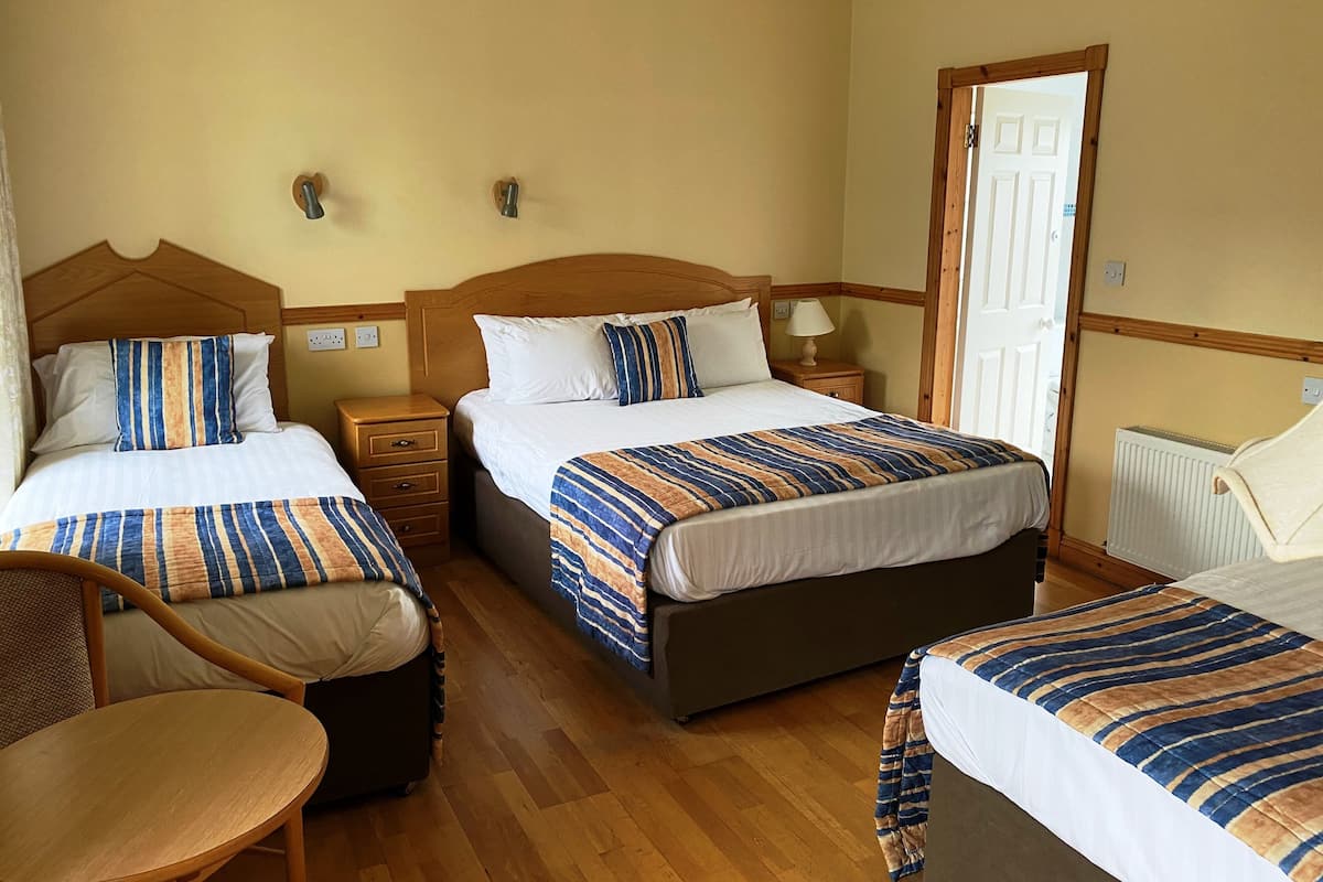 Una habitación de hotel con dos camas individuales, una silla de madera, una mesita pequeña y un radiador.