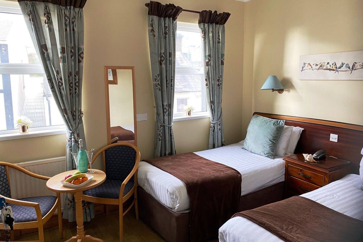 Habitación de hotel con dos camas, una silla, una mesita con un plato de fruta y una lámpara.