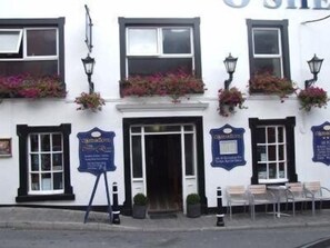 A white building with black-framed windows, flower boxes on the upper windows, and a signboard on the wall. - O'Sheas Hotel Tramore (Tramore)