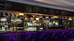 Un bar con piso a cuadros, una barra con diferentes botellas y vasos, y un letrero que dice "Members Only".