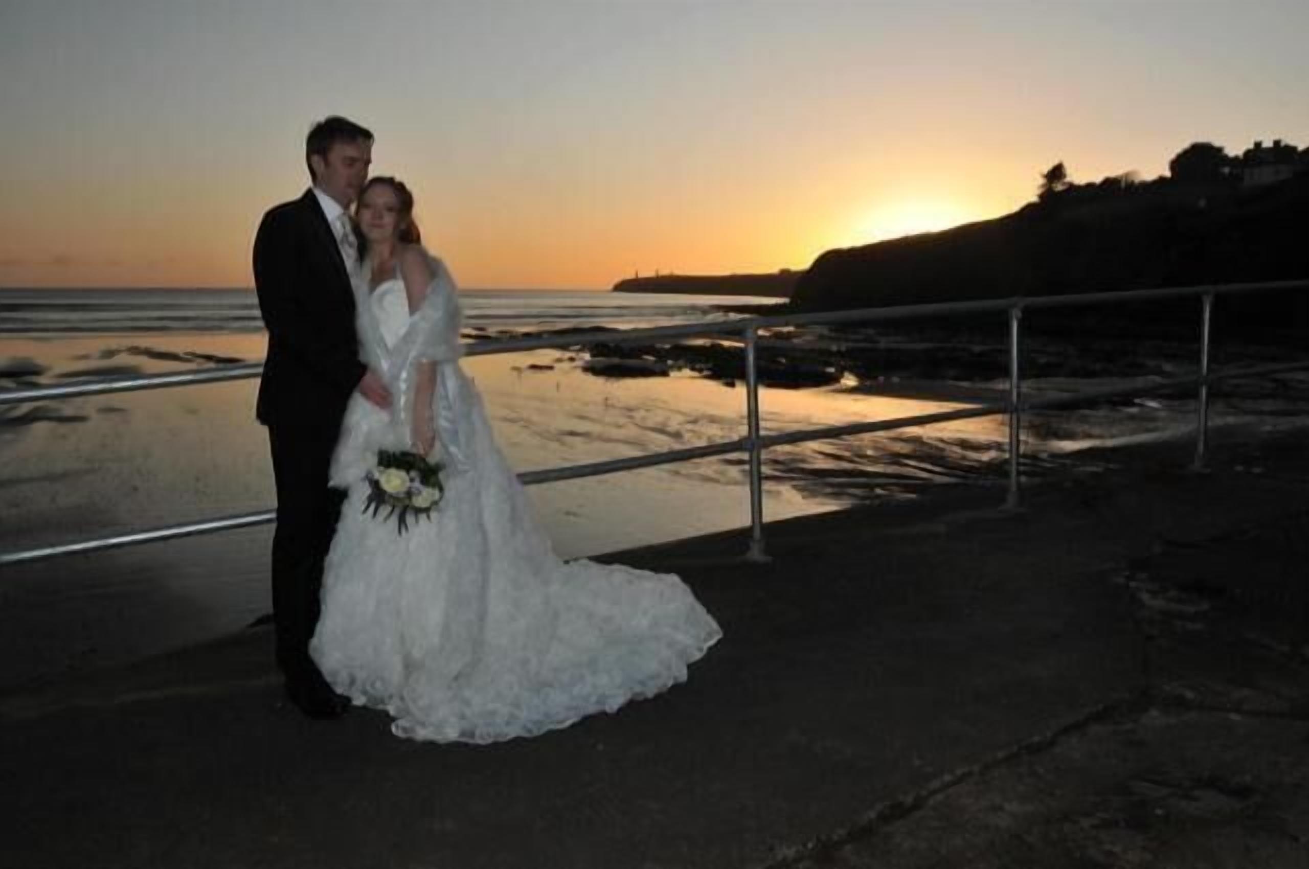 A couple standing on a balcony with a sunset view.