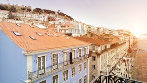 Un edificio de varios pisos con balcones y tejado de tejas rojas, con vistas a una calle con gente caminando.