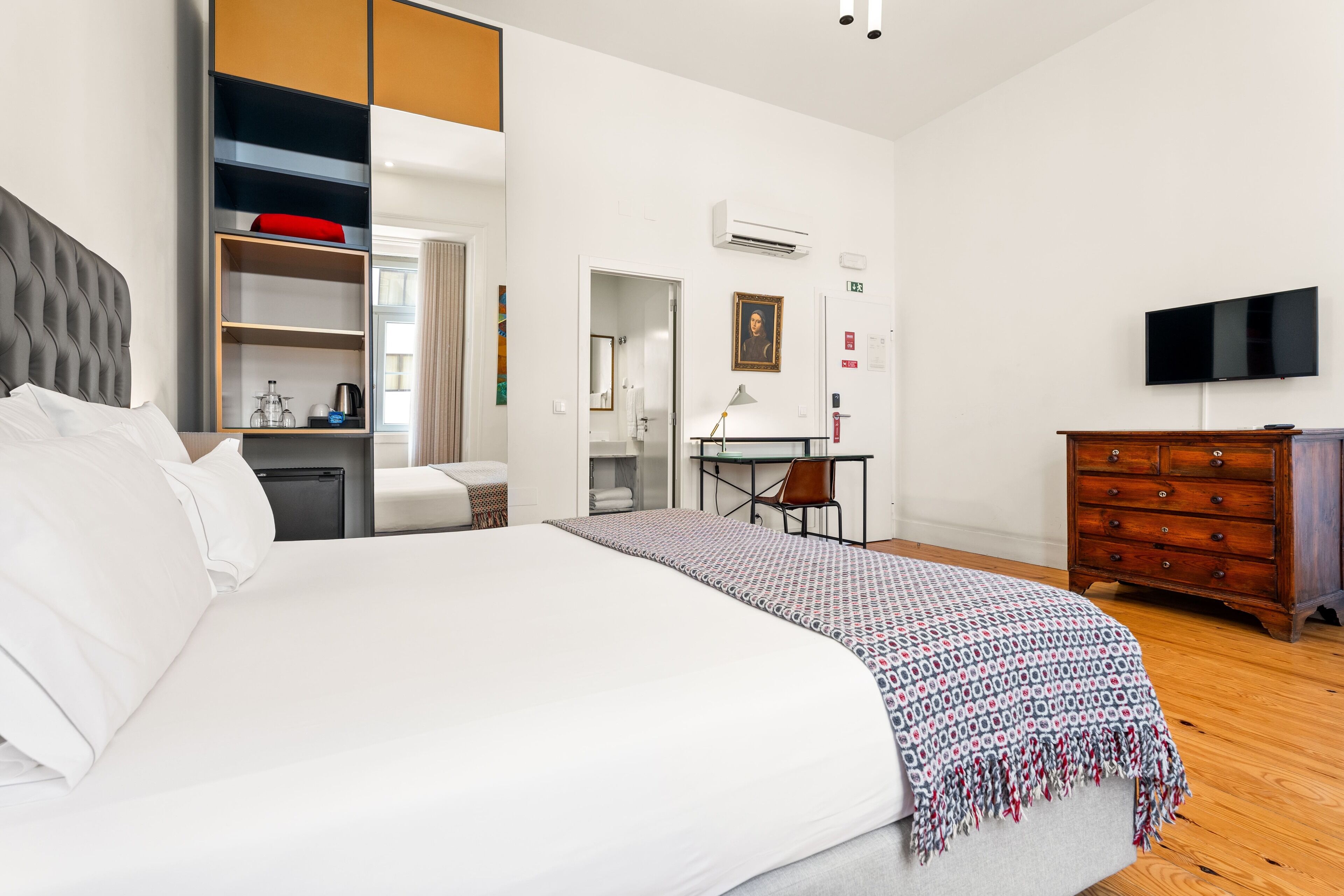 A hotel room with a large bed, a desk, a chair, a dresser, and a television.