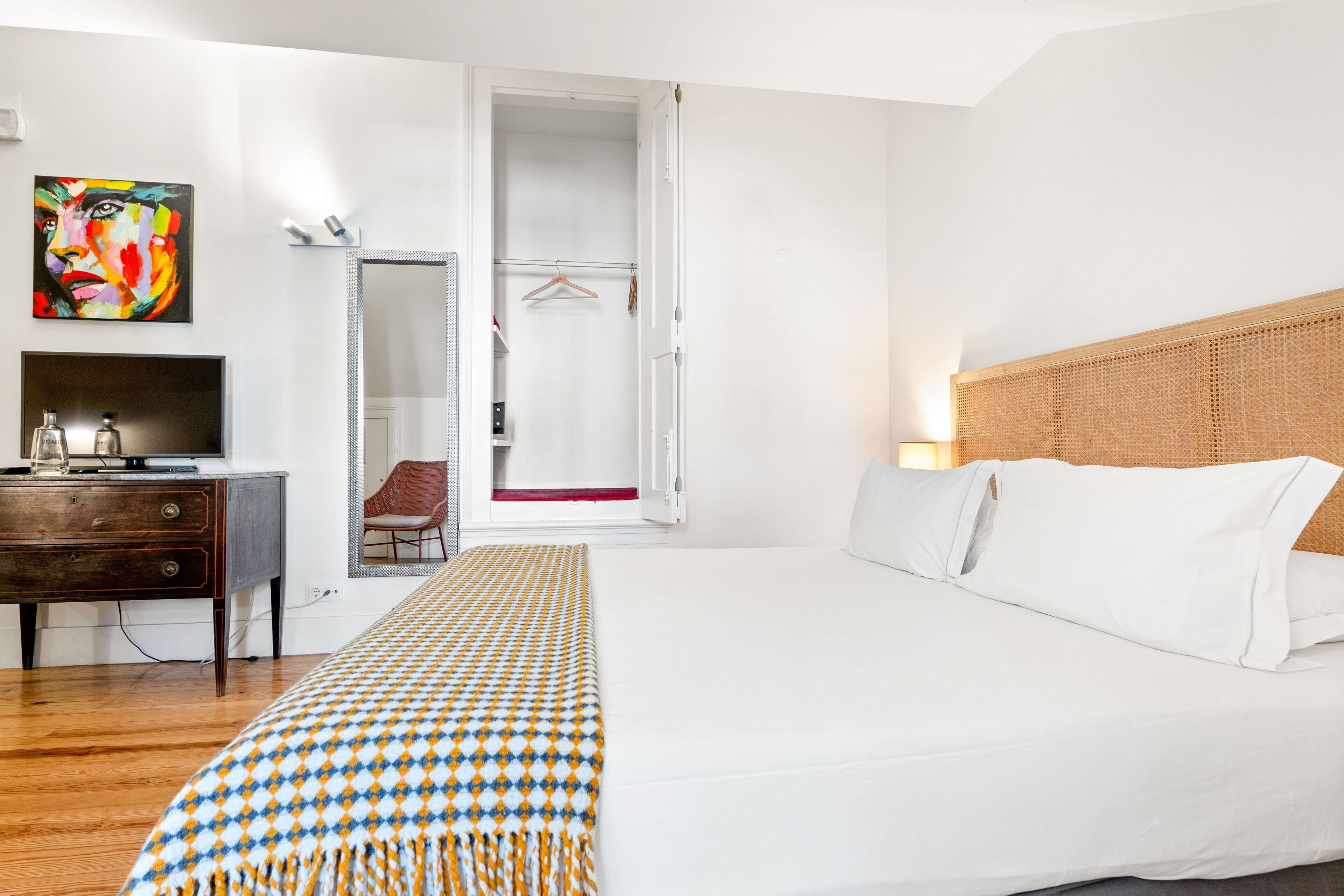 Habitación de hotel con cama, escritorio con televisor, armario y un cuadro en la pared.