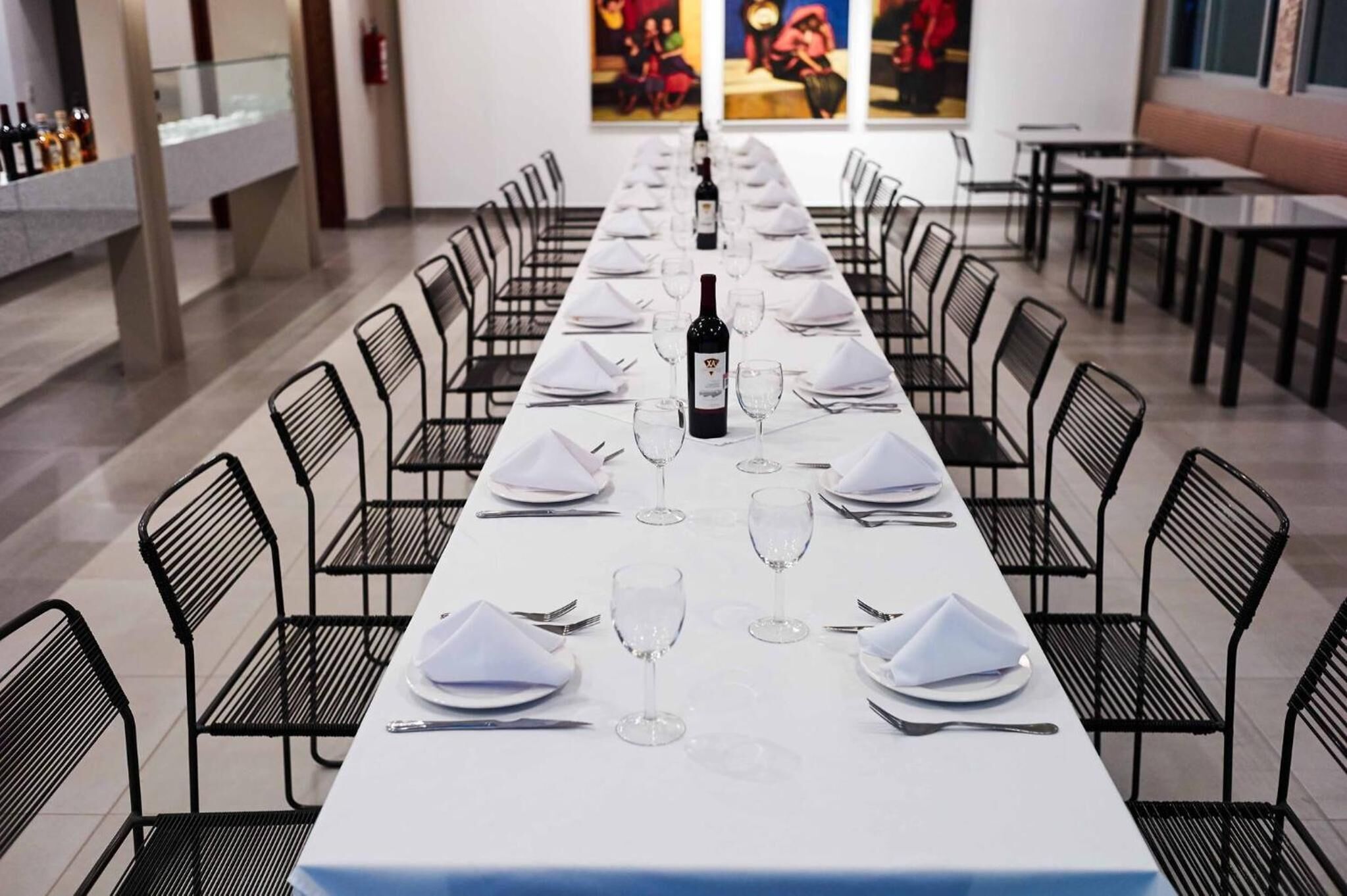 Une longue table de salle à manger rectangulaire, recouverte de nappes blanches, agrémentée de serviettes pliées et de verres à vin, et entourée de chaises noires.