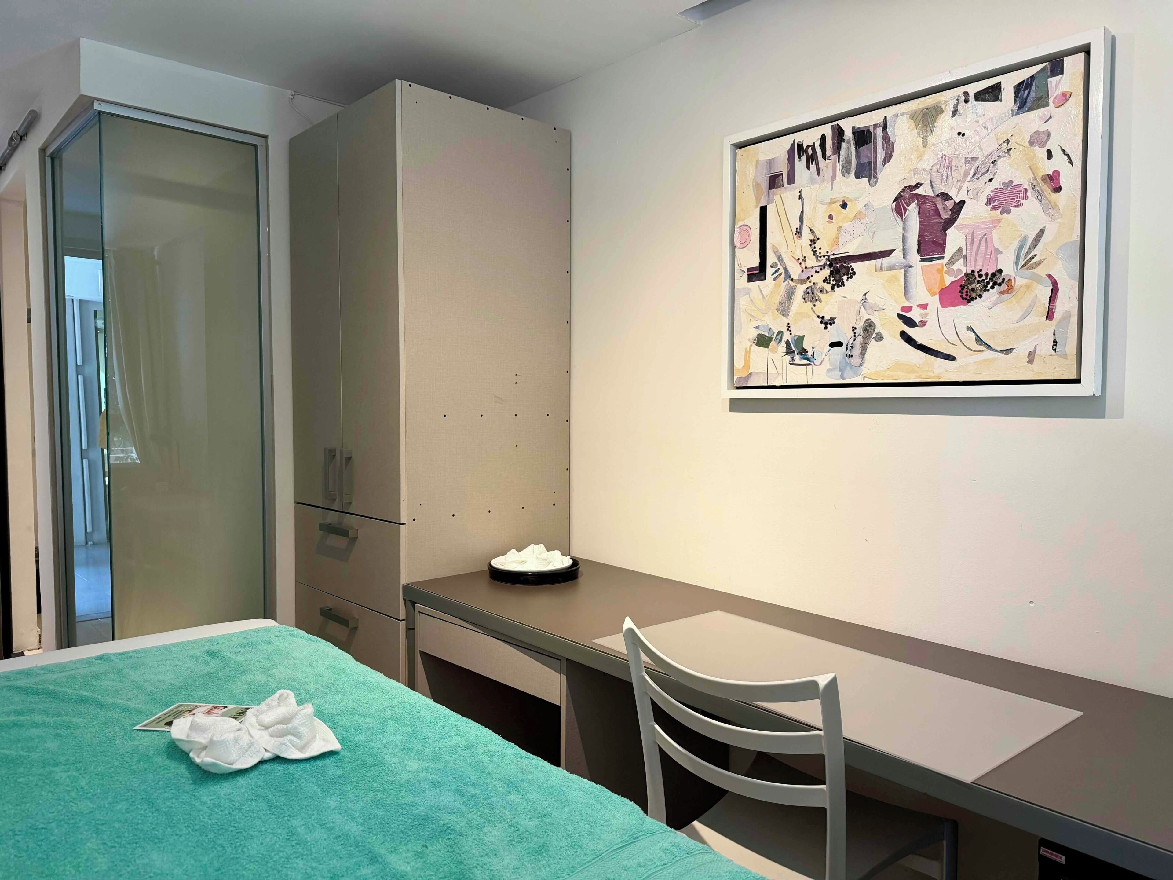 Een kamer met een bed, een bureau, een stoel, een kledingkast en een schilderij aan de muur.