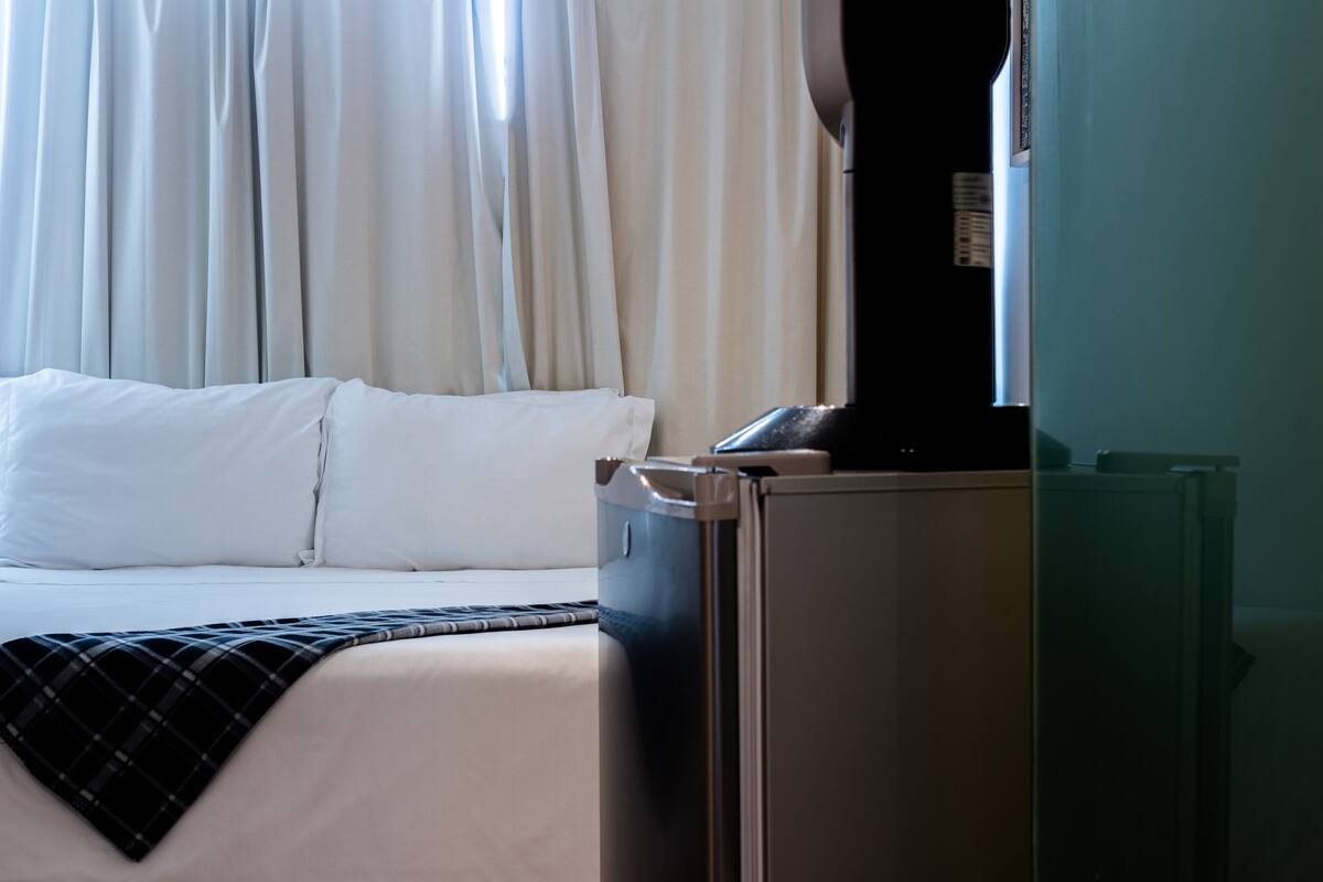 A hotel room with a bed, a flat-screen TV, and a refrigerator.