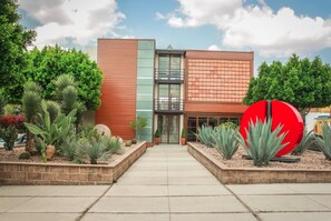 Un edificio moderno con entrada de vidrio, rodeado de jardines ajardinados y una gran escultura roja.