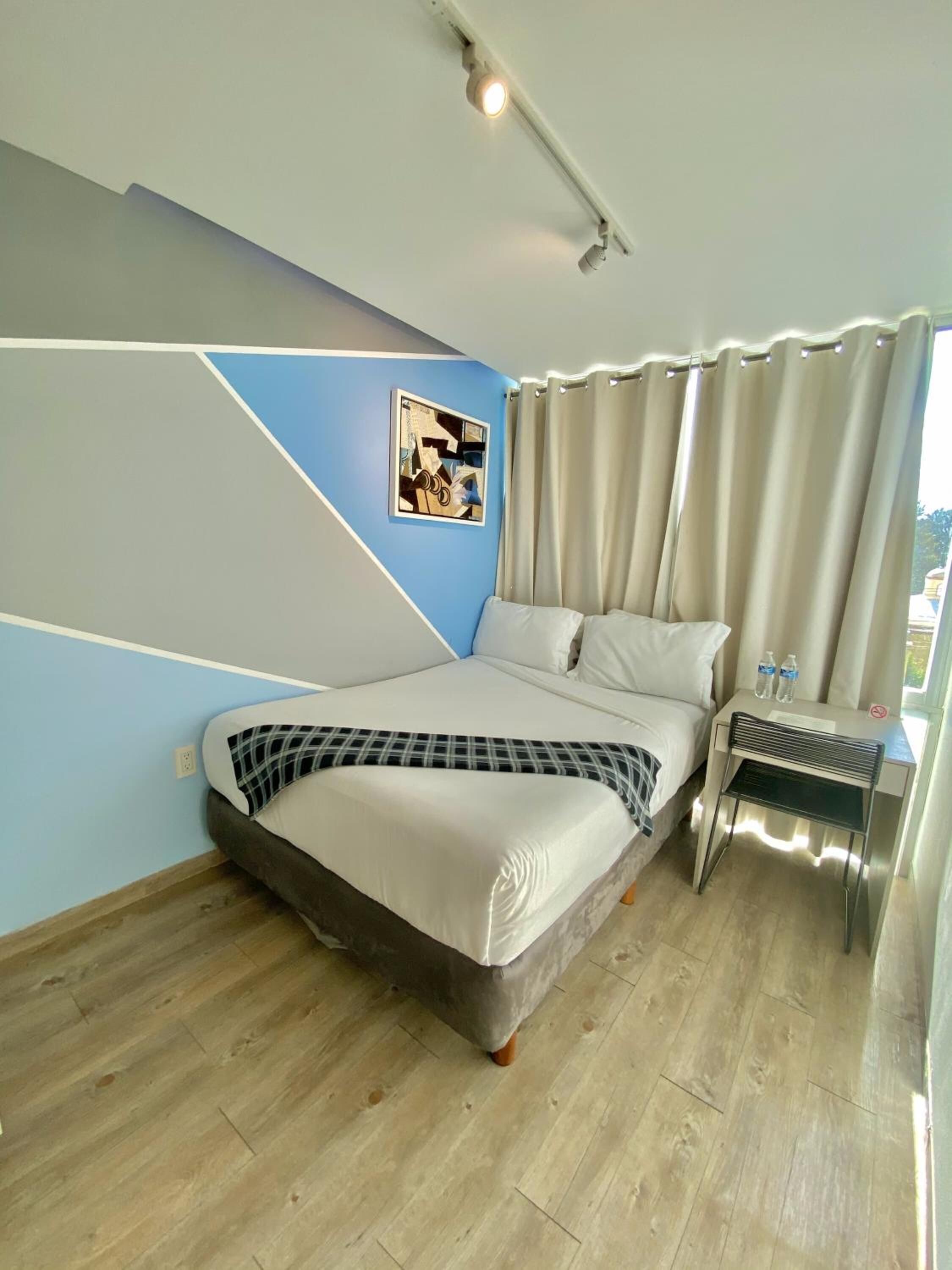 A modern bedroom with a bed, a desk, and a window with curtains.