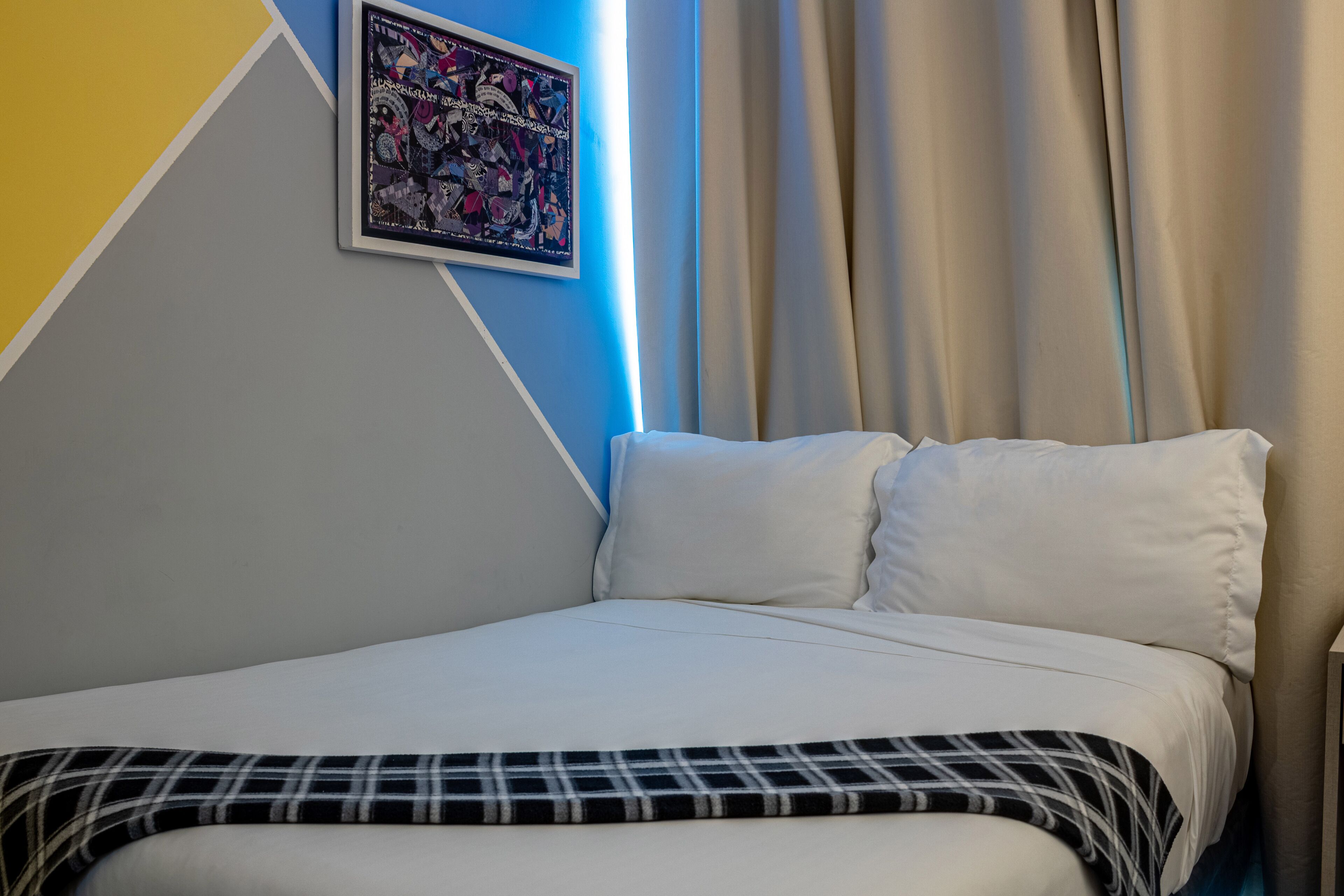 A neatly made bed with a plaid bedspread, a framed picture on the wall, and a window with curtains.
