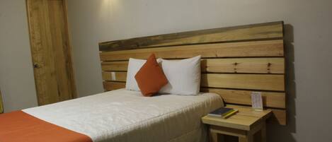 A neatly made bed with a wooden headboard, a small bedside table with a book, and a wall-mounted light fixture.
