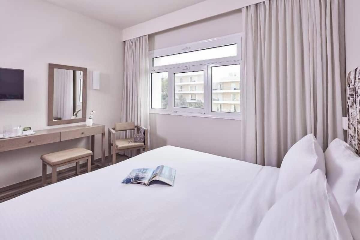 A hotel room with a bed, a desk, a chair, a window, and a mirror.