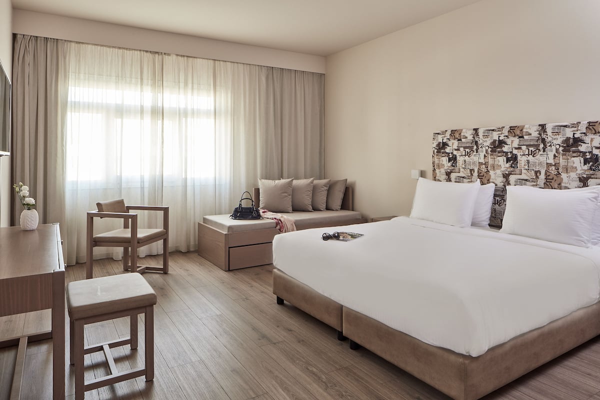 A hotel room with a large bed, a desk, a chair, a small table, and a nightstand.