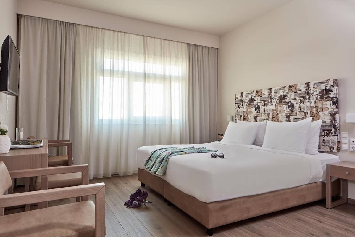 A hotel room with a large bed, a desk, a chair, and a television.