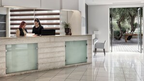 Uma área de recepção moderna com balcão de mármore, divisórias de vidro e vista para um deck externo com árvores.