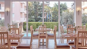 Uma sala de jantar com mesas e cadeiras dispostas para o atendimento, grandes janelas com vista para edifícios e áreas verdes ao redor.