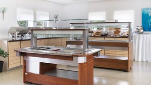 Disposição de buffet com vitrines de vidro, um canto para café e uma mesa com acompanhamentos.