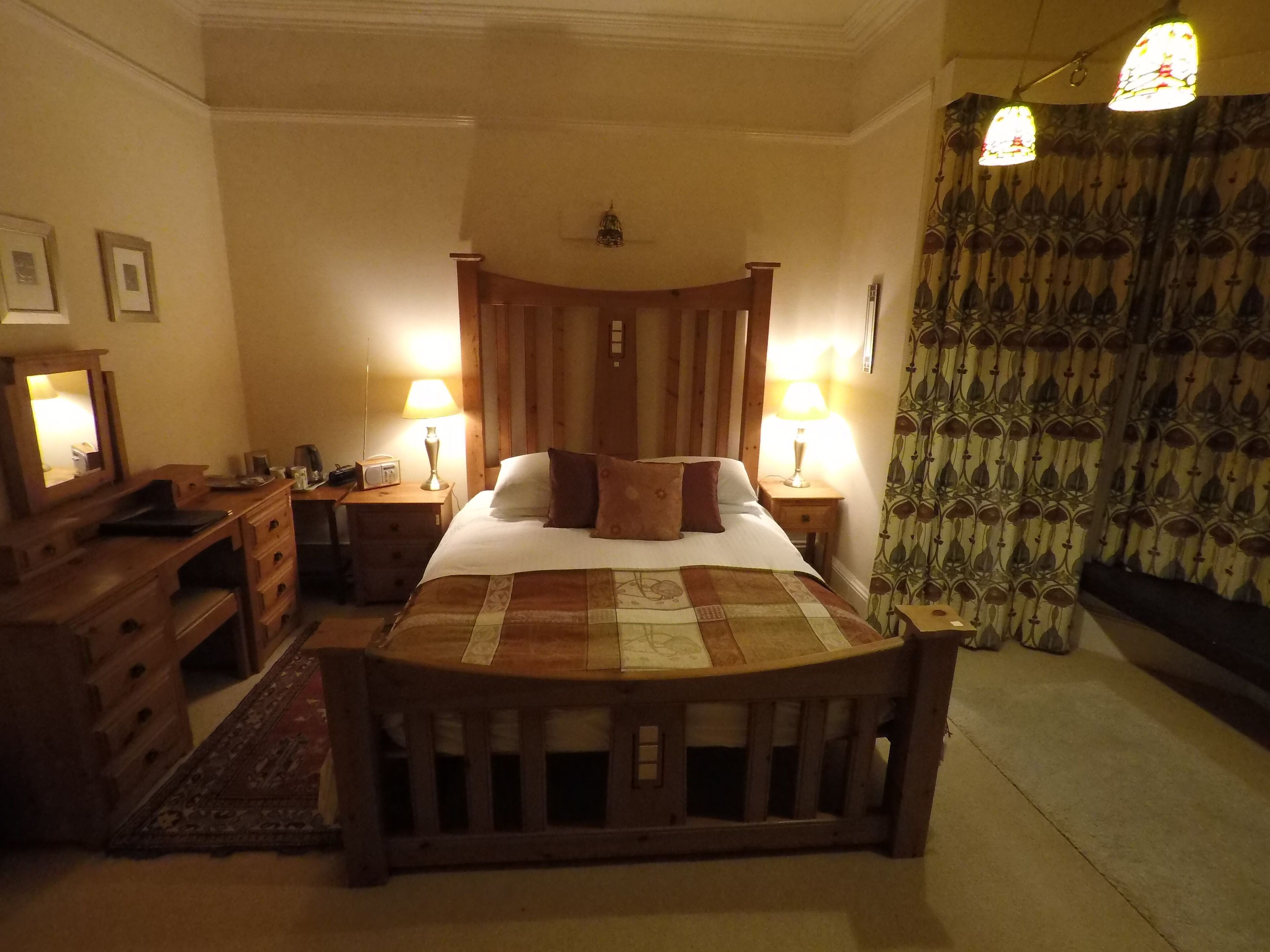 Un dormitorio tradicional con una cama de madera con dosel, dos mesitas de noche con lámparas, un aparador y una cortina estampada.